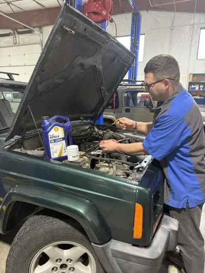 Mechanic holding new oil and filter beside engine bay of a 2000 Jeep Cherokee Sport during oil change service